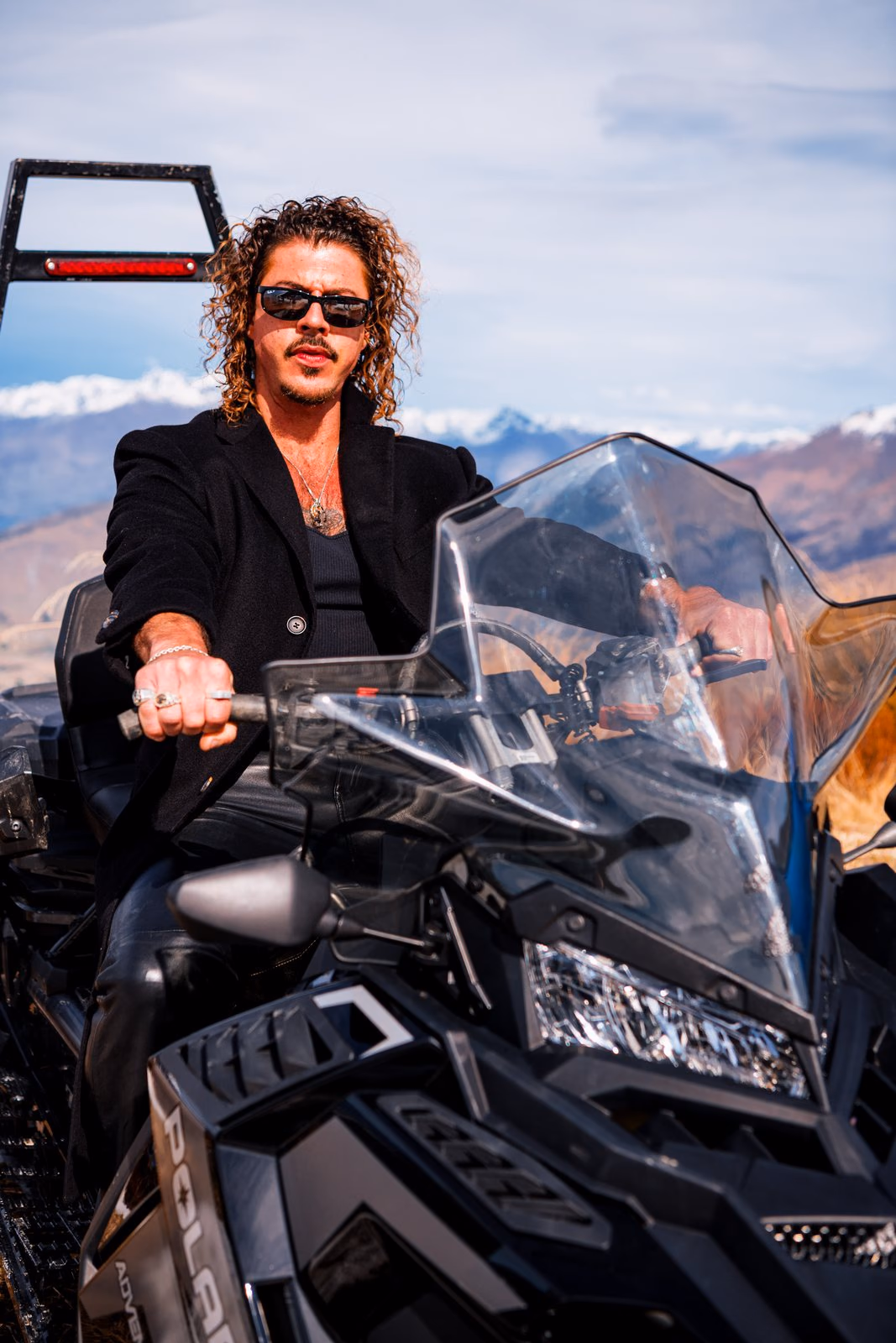 Keli Holiday on a black Polaris snowmobile with snow-capped mountains behind